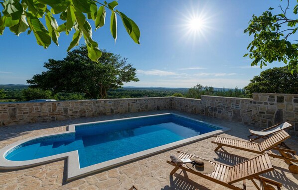 A swimming pool with stone walls and lounge chairs, surrounded by greenery and a clear sky. - Pet friendly home in Benkovac (Benkovac)