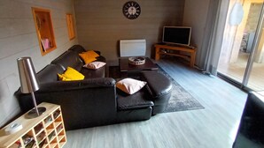 Ein Wohnzimmer mit einer schwarzen Ledersofa, einem Holztisch, einer Wanduhr und einem Fernseher auf einem Schrank.
