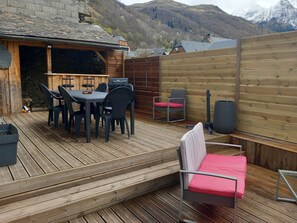 A wooden deck with a table and chairs, a barbecue grill, and a seating area with cushions. - Loudenvielle Family Center (Loudenvielle)