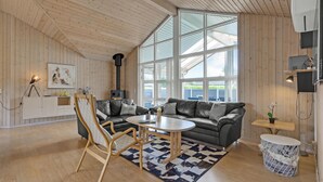 Een gezellige woonkamer met een groot raam, een open haard, een bank, een bijzettafeltje en een houten plafond.