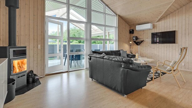 Een moderne woonkamer met een zwart houtkachel, een grijze bank en een aan de muur bevestigde televisie.