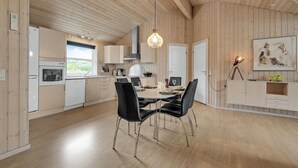 Een moderne keuken met houten lambrisering, een eetgedeelte met zwarte stoelen en een hanglamp.
