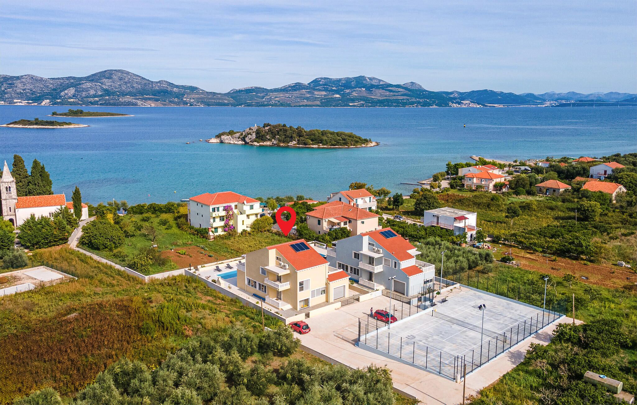 Un quartier résidentiel situé sur la côte, avec des bâtiments modernes, une église et une vue sur la mer et les montagnes.
