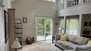 A spacious living room with a high ceiling, large windows, a ceiling fan, and a staircase leading to an upper level. - Bay view from Calvert Cliffs, Solomons Island & State Park nearby (Lusby)