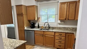 A kitchen with wooden cabinets, a granite countertop, a stainless steel sink, and a window with a view of trees. - Bay view from Calvert Cliffs, Solomons Island & State Park nearby (Lusby)