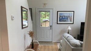 A hallway with a wooden floor, a white door with a window, a white sofa, a small table with a vase, and framed pictures on the walls. - Bay view from Calvert Cliffs, Solomons Island & State Park nearby (Lusby)