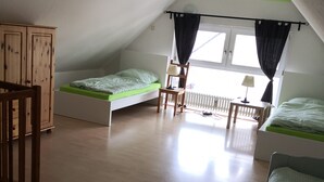 A spacious attic bedroom with a high ceiling, two single beds, a wooden wardrobe, a chair, a table, and a radiator. - Vacation apartment in a beautiful location between 2 lakes for 2-6 people (Malente)