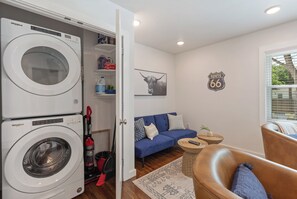 A compact living space with a front-loading washer and dryer, a blue sofa, a small side table, and a Route 66 sign on the wall.