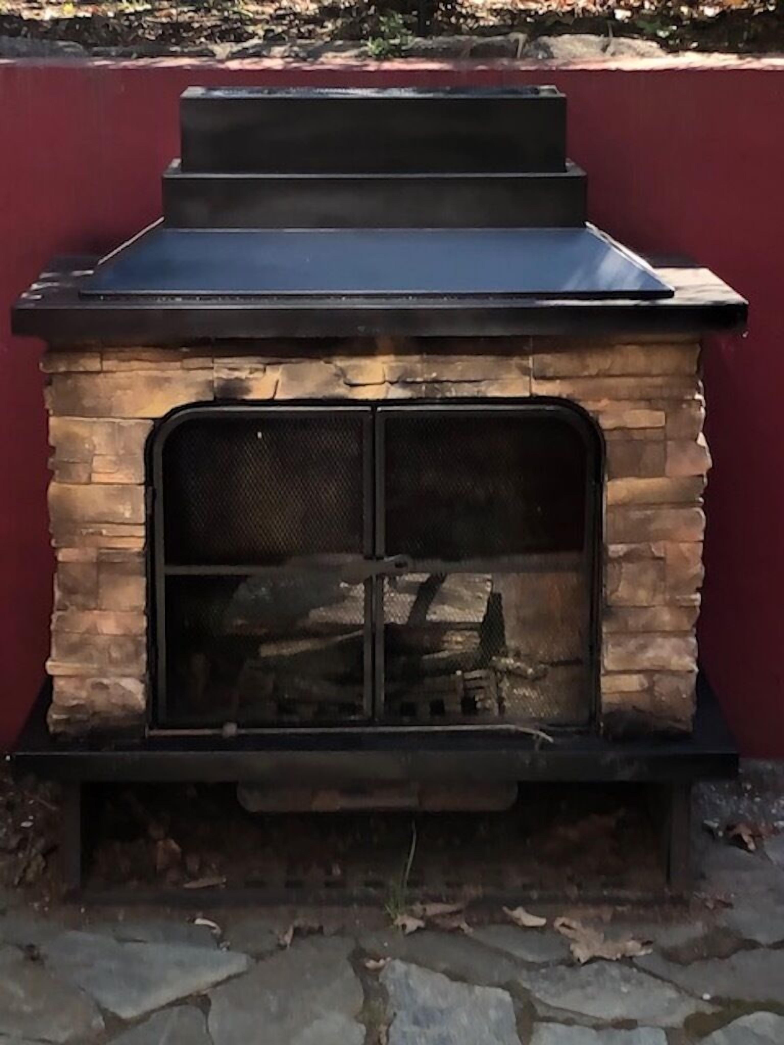 A stone-built outdoor fireplace with a metal top and a mesh front.