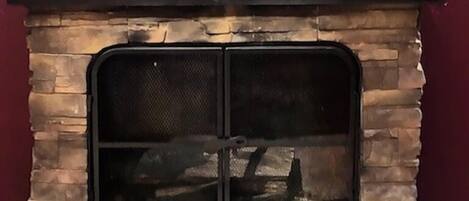 A stone-built outdoor fireplace with a metal top and a mesh front.
