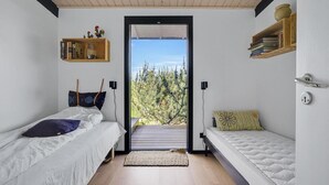 Een compacte slaapkamer met twee bedden, een houten plafond en uitzicht op bomen door een groot raam.