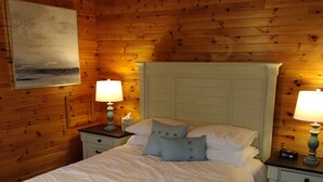 A wooden-paneled bedroom with a bed, nightstands, and a painting on the wall. - Eastern Beacon Inn Room 3 (Lubec)