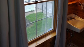 A bathroom with a window, wooden walls, a sink, and a mirror. - Eastern Beacon Inn Room 3 (Lubec)