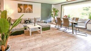 A living room with a sofa, coffee table, dining table with chairs, and a large window with a view. - Nice apartment in Marienmünster (Marienmünster)