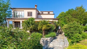 A two-story house with a stone pathway leading to the entrance, surrounded by lush greenery and a clear blue sky. - Gorgeous home in Jadranovo (Jadranovo)