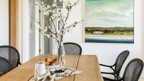A dining table with a vase of flowers, a pitcher, and a bowl of bread. There is a painting of a landscape on the wall behind the table. - Private Hilltop Chilmark Estate with private tennis court, gym and hot tub (Chilmark)