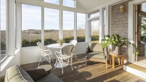 A sunlit room with large windows, wicker furniture, and a view of the outdoors. - Private Hilltop Chilmark Estate with private tennis court, gym and hot tub (Chilmark)