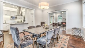 Un comedor amplio con una gran mesa de madera y sillas cómodas, una cocina moderna al fondo, y vista al salón.