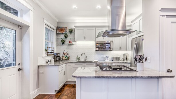 Una cocina moderna con armarios blancos, una isla central, electrodomésticos de acero inoxidable y un ventanal con detalles decorativos.