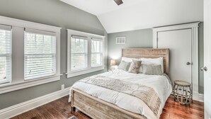 Un dormitorio con una cama grande, un ventilador de techo y tres ventanas con persianas.