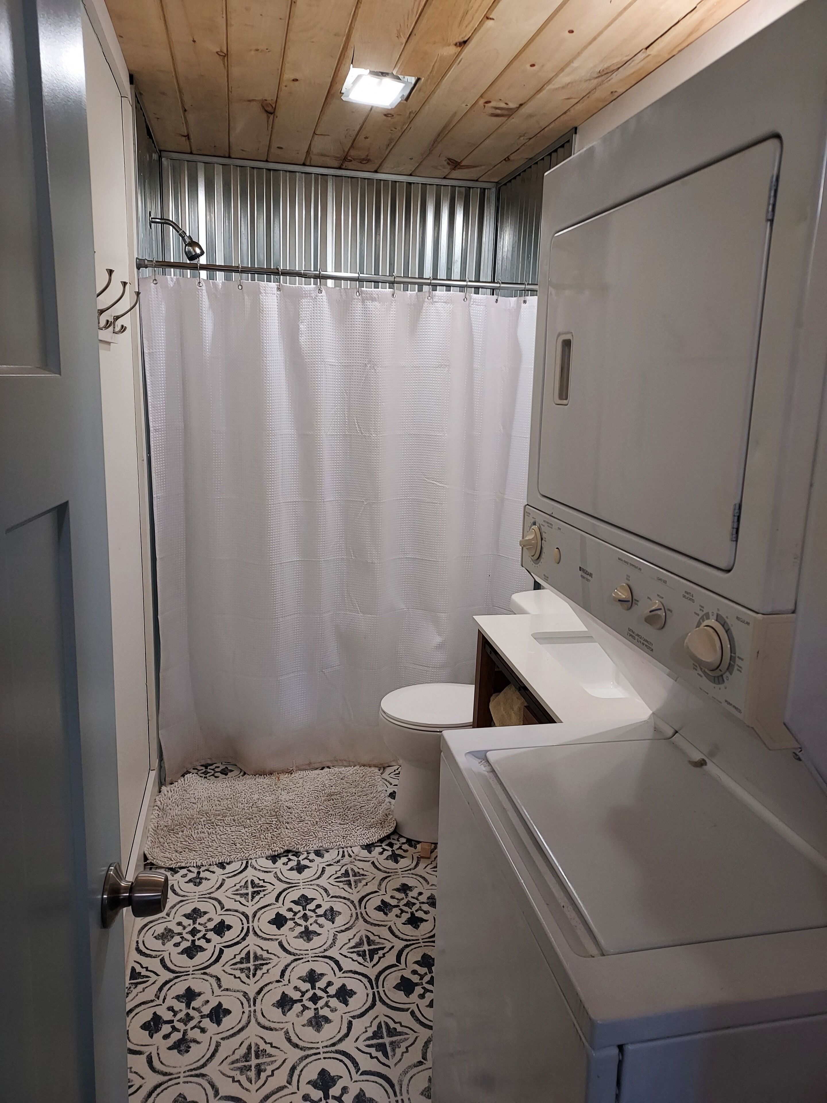 Un bagno compatto con tenda doccia, water e lavatrice a scomparsa.