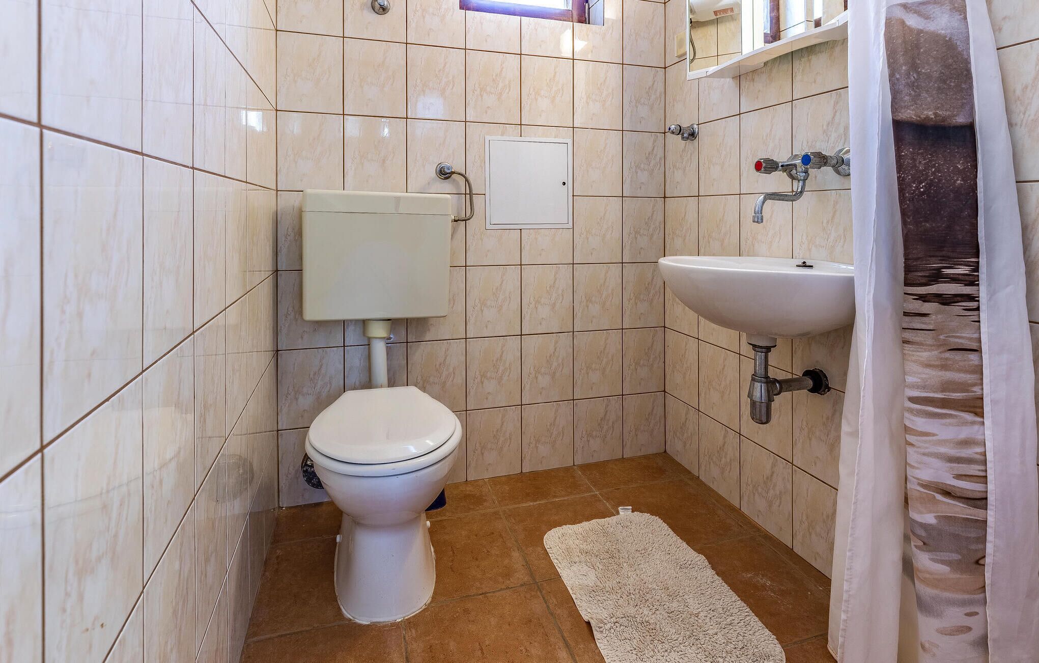 Et lille badeværelse med toilet, vask og bruseforhæng.