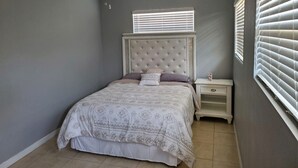 Un dormitorio con cama, mesita de noche, ventilador de techo y ventana con persianas.