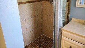 Un baño pequeño con azulejos color beige, una cortina de ducha y un lavamanos con espejo.