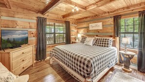 Une chambre dans un chalet en rondins, avec un grand lit, une commode en bois et un téléviseur posé sur une autre commode.
