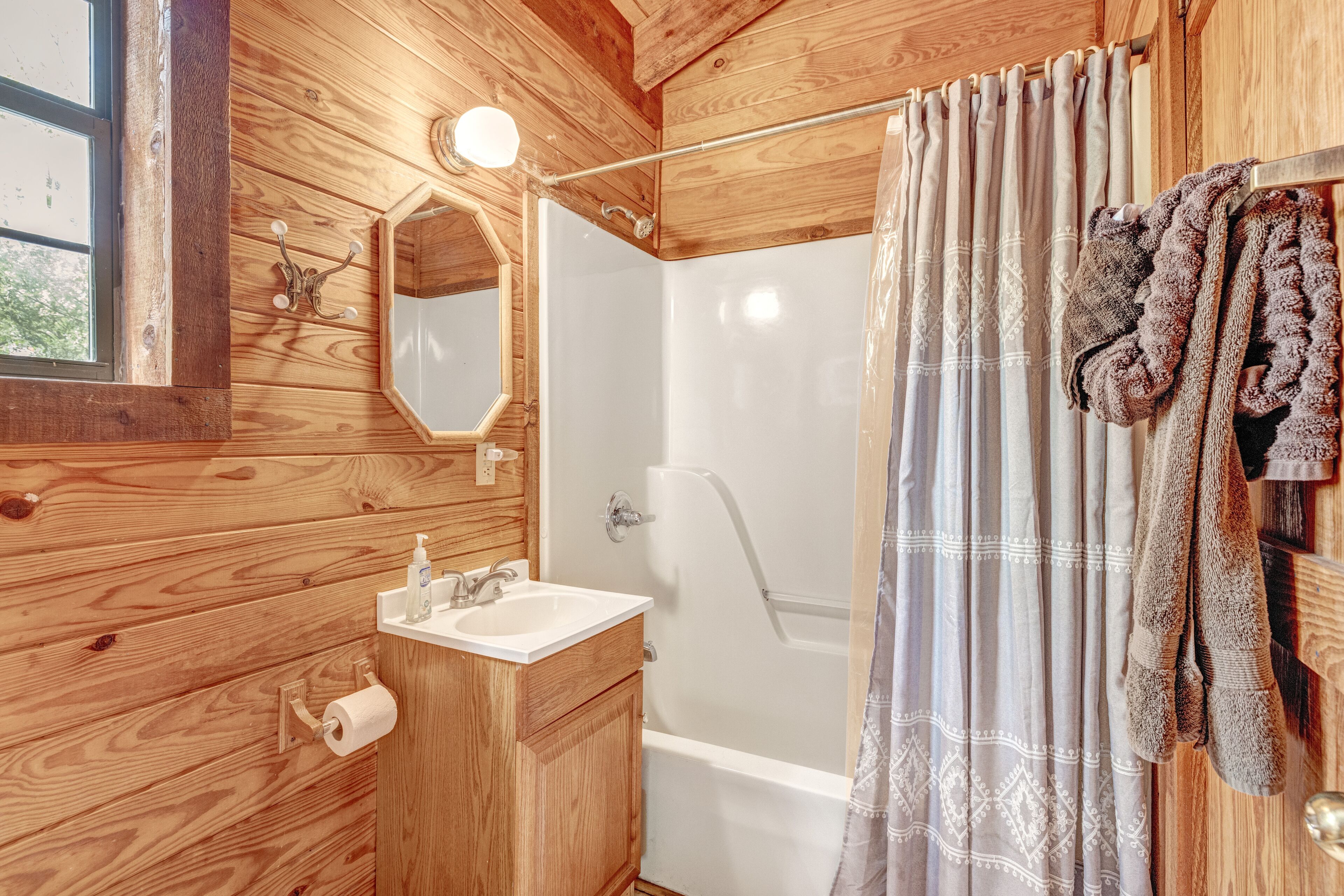A wooden cabin bathroom with a sink, mirror, and shower.
