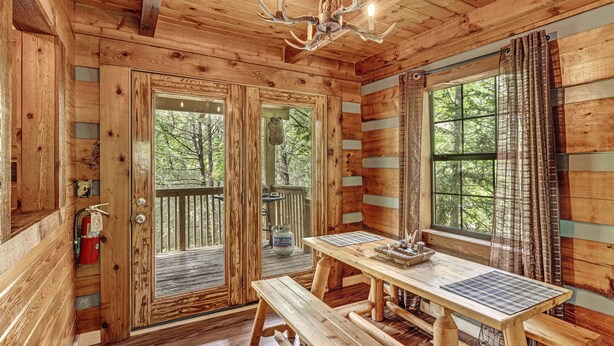 L’intérieur d’un chalet en bois, avec une table en bois, des bancs, un lustre et de grandes fenêtres ornées de rideaux.