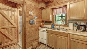 Une cuisine rustique aménagée dans une cabane en bois, avec un poêle, un évier et des placards.
