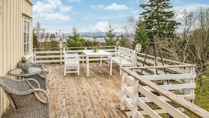 A wooden deck with white railings, wicker furniture, and a table with a bowl of flowers. - Amazing home in Ytterøy with WiFi (Ytterøy)