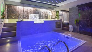 En moderne swimmingpool indendørs med et klart vandfald, et blåt lysloft og en baggrundsvæg i sten.