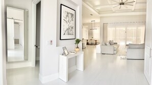 Un espacio habitable amplio con una estética moderna en blanco, que incluye un conjunto de sofás, una consola con una planta en maceta y una obra de arte enmarcada en la pared.
