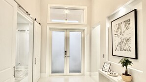 Un pasillo con un par de puertas, un cuadro en la pared y una mesita con una planta.