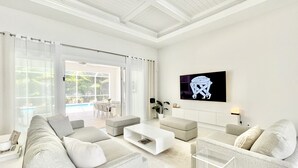 Un salón moderno con una televisión grande, asientos cómodos y vistas a una piscina.