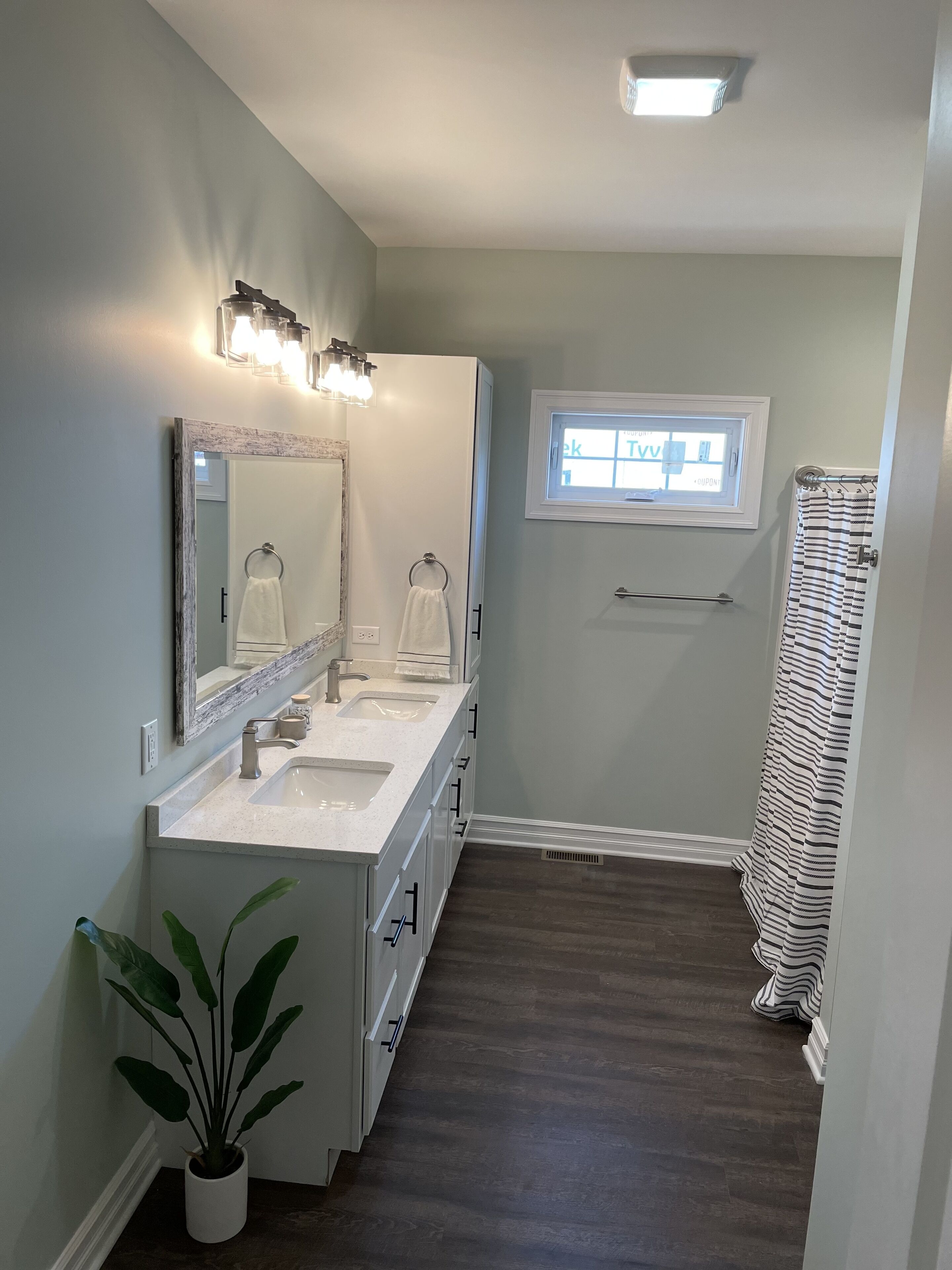Une salle de bain avec un meuble-lavabo à deux vasques, un grand miroir, une fenêtre et une douche avec un rideau à rayures.