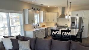 Une cuisine moderne avec des meubles blancs, un réfrigérateur en acier inoxydable et un coin repas comprenant une table et des chaises.