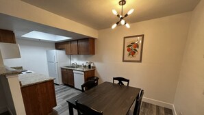 Une cuisine de taille réduite avec des meubles en bois, un réfrigérateur blanc, une table à manger avec quatre chaises et un luminaire suspendu au plafond.