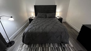 Une chambre à coucher avec une tête de lit sombre, une couvre-lit matelassée, deux tables de chevet avec des lampes et un tapis à rayures.