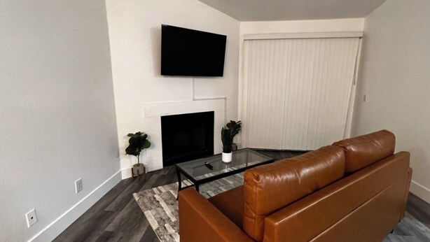 Un salon moderne avec un canapé en cuir marron, une table basse en verre, un téléviseur à écran plat fixé au mur et une cheminée.