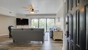 A spacious living room with a gray sofa, a flat-screen TV, and a ceiling fan. - Newly Renovated 2BR/2BA Flat/3 Smart TV’s/WIFI/Pool & Tennis/Pickleball Views (Hilton Head Island)