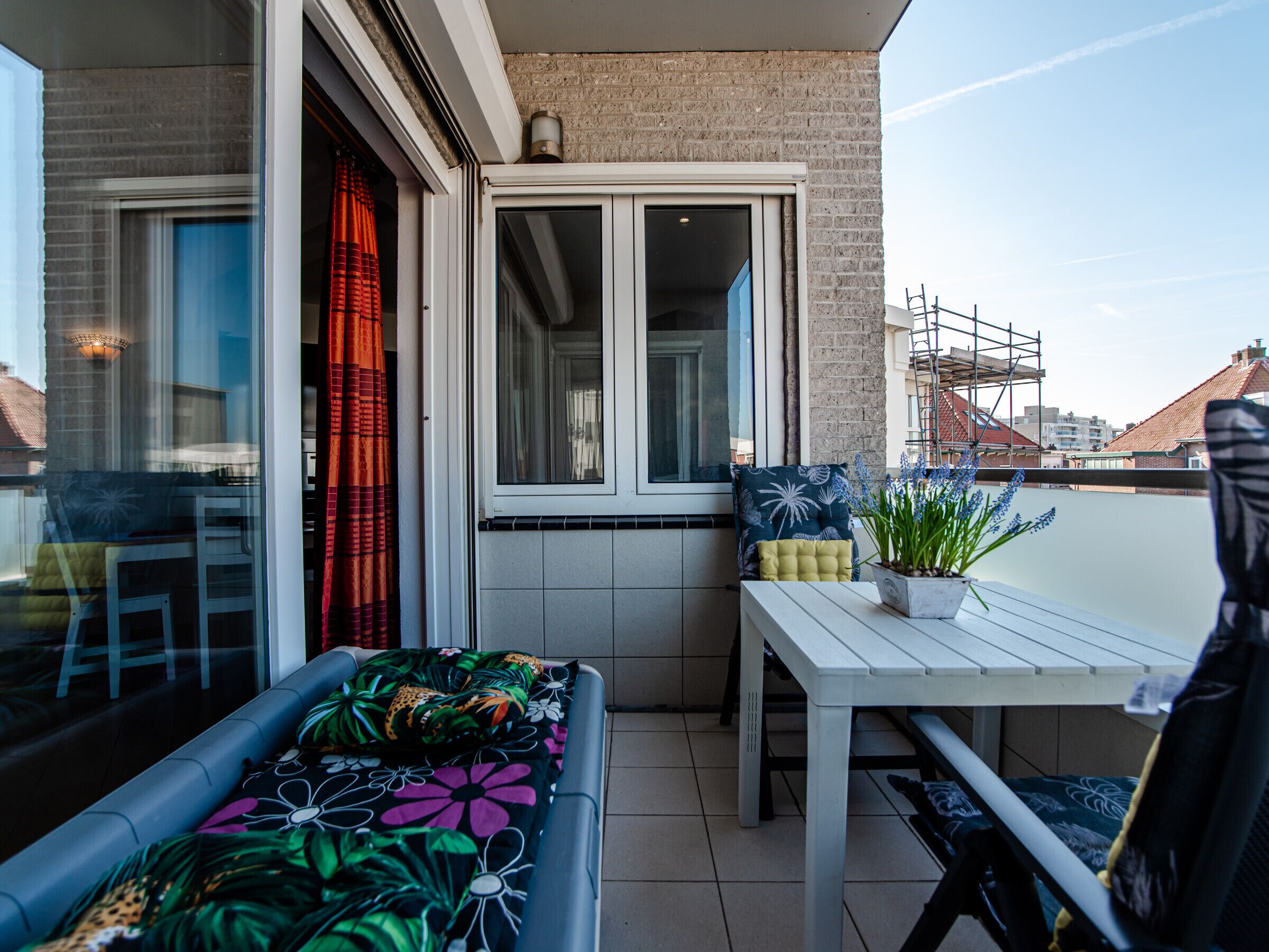 Ein Balkon mit einem weißen Tisch und Stühlen, einer Couch mit floralem Bezug und einem Topfpflanzen.