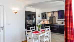 Una cocina compacta con electrodomésticos modernos, un comedor con una mesa y sillas blancas, y una cortina roja.