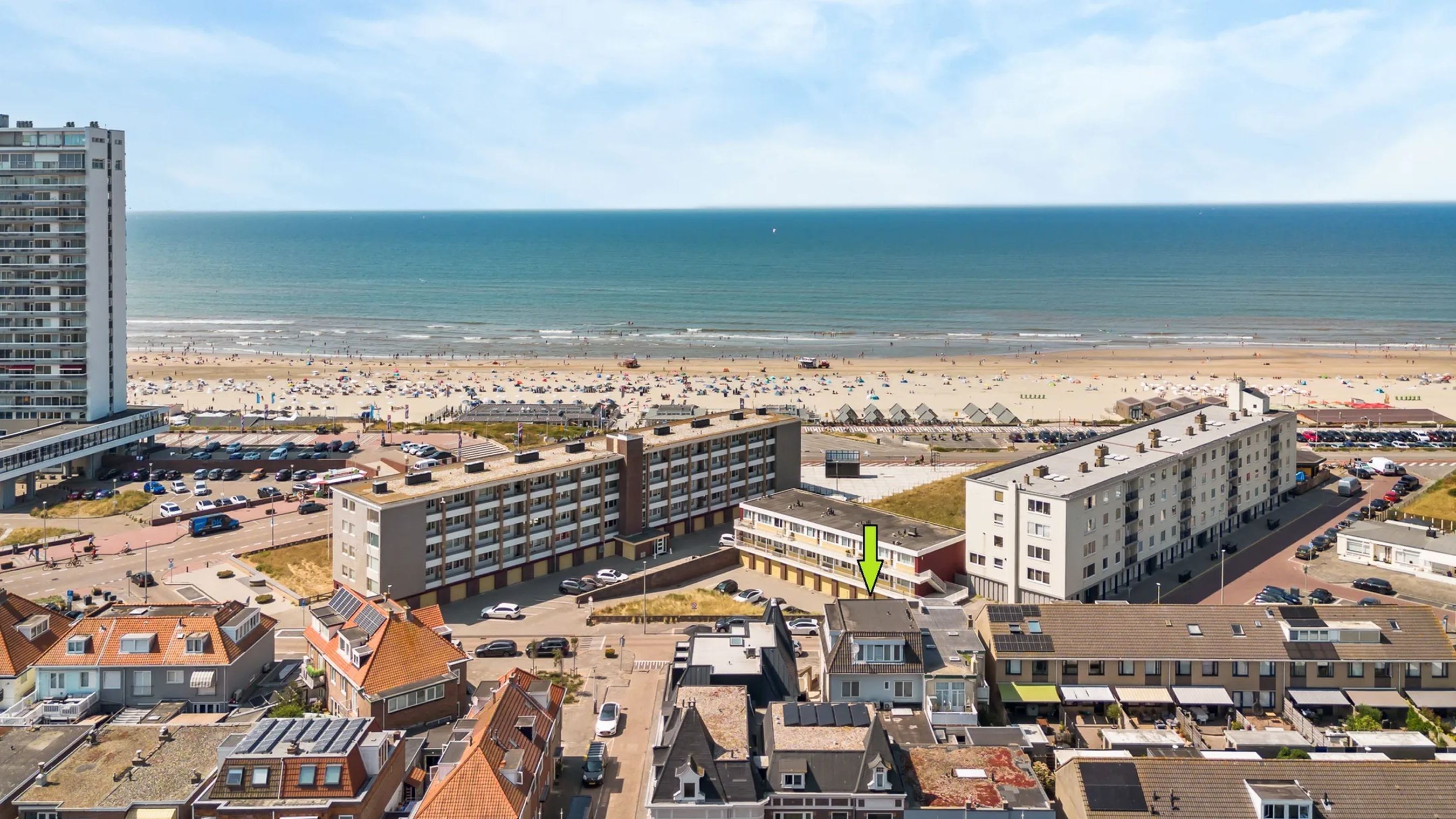 Une zone urbaine côtière avec une plage, de nombreux bâtiments et des voitures garées.