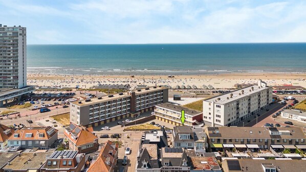 A coastal urban area with a beach, multiple buildings, and parked cars.