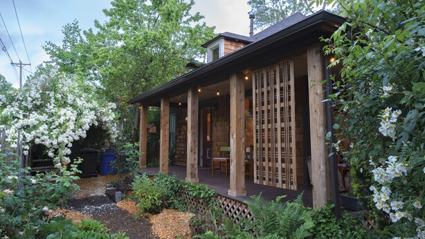 A wooden house with a porch, surrounded by lush greenery and flowering plants. - Entire Home in Downtown Eugene (Eugene)