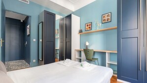 Ein modernes Schlafzimmer mit Bett, Schreibtisch und Stuhl. Regale mit Dekoration und eine Tür zu einem anderen Raum.