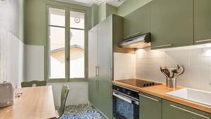 Eine kleine Küche mit grünen Schränken, einer Holzarbeitsplatte und einem Fenster mit Blick auf ein Haus.